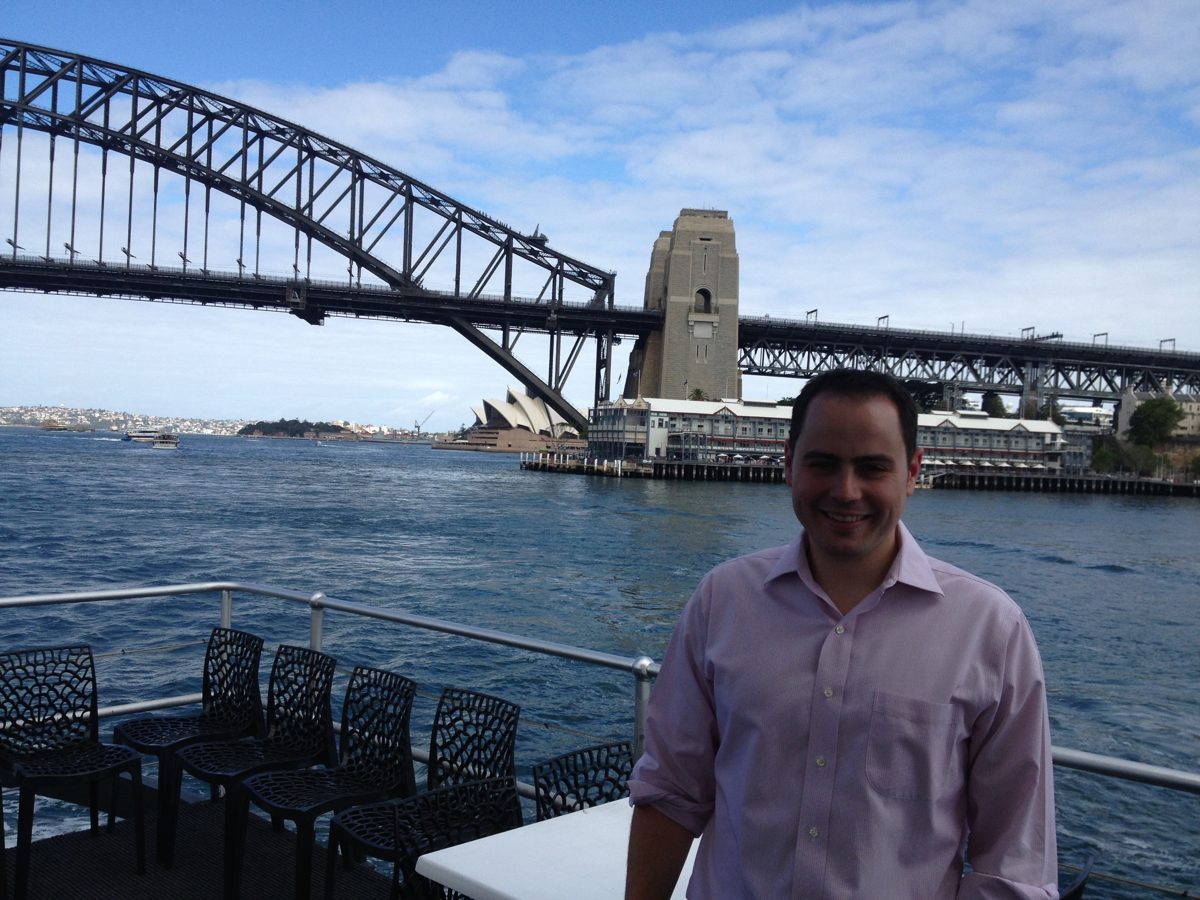 Michael on a ferry deck in Sydney Harbour, with the Harbour Bridge and Opera House behind him
